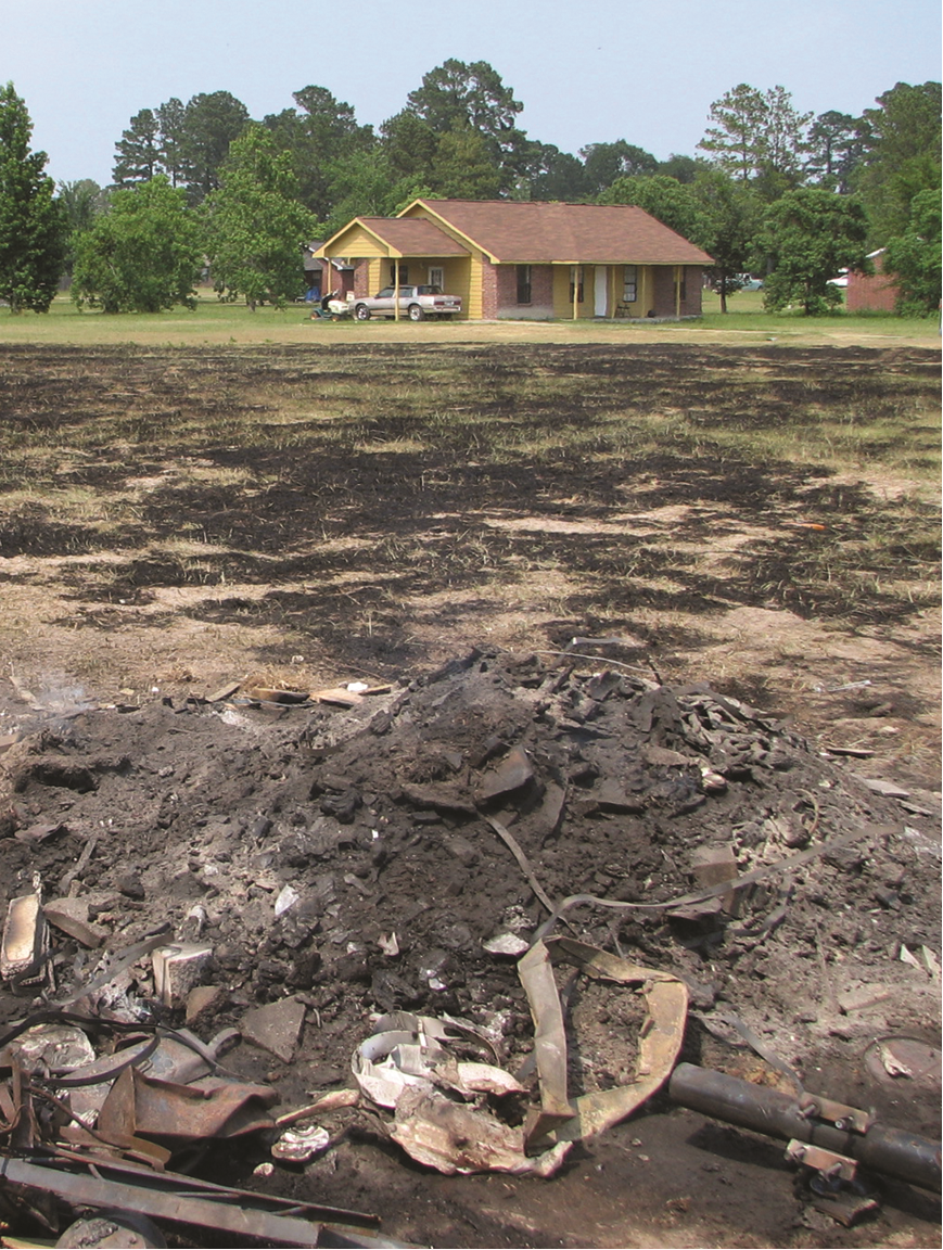 Burned field and debris in front of house.