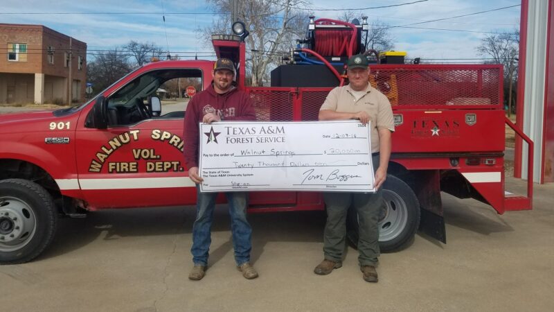 A red Walnut Springs Volunteer Fire Department truck holding a large ceremonial check from the Texas A&M Forest Service for $20,000.