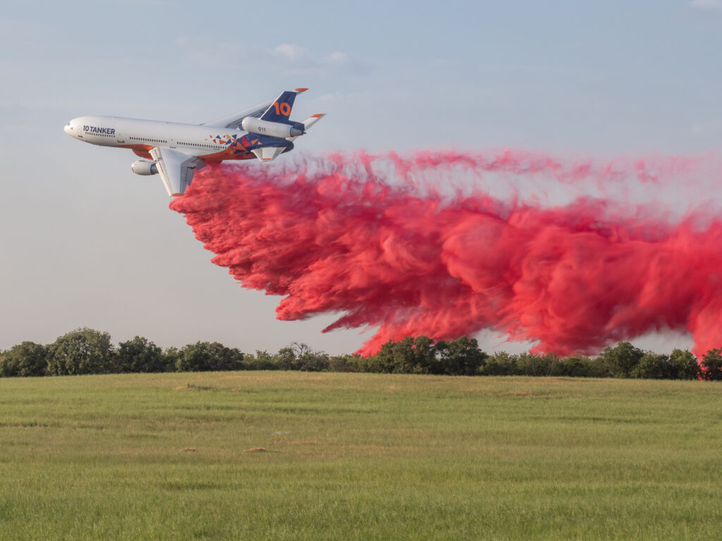 Plane drops red retardant over green field