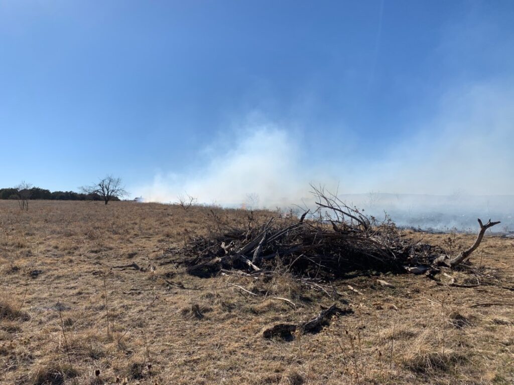 Large brush pile with smoke in the background