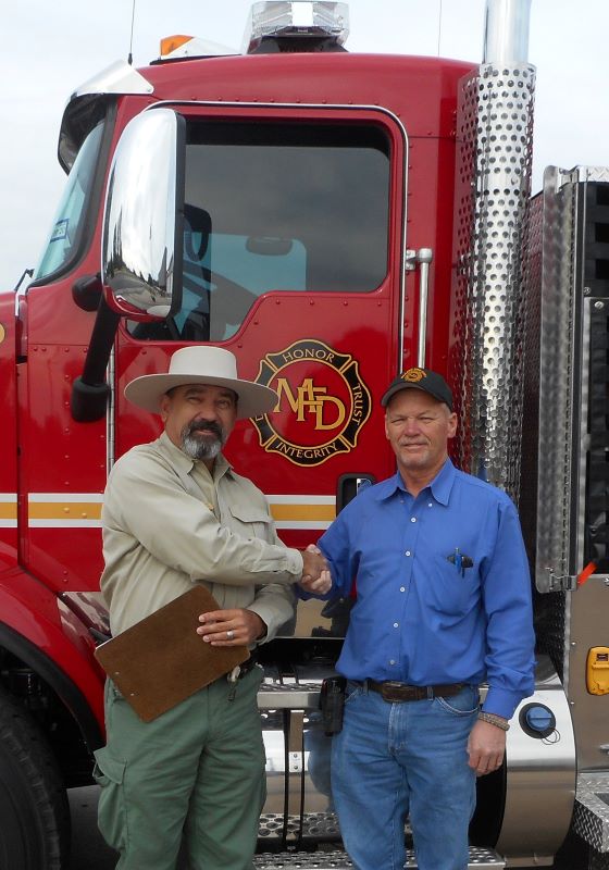 Two men shaking hands in front of fire truck
