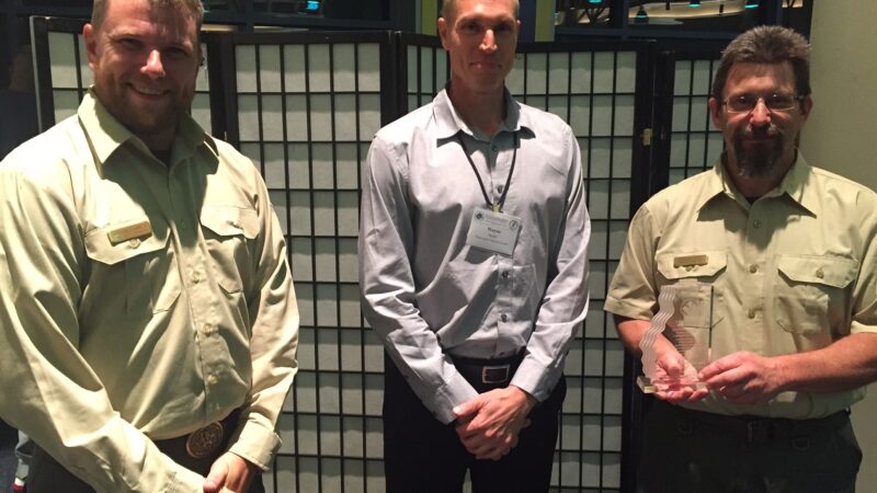 Three men stand smiling