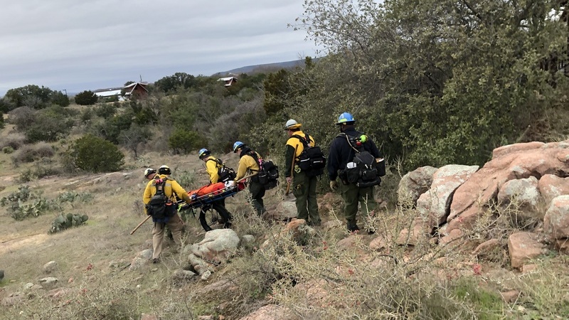 firefighters working together to carry a dummy on a stretcher down a rocked hill