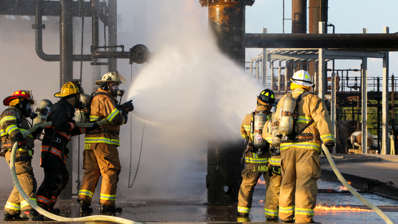 Two groups of firefighters spring a tall metal beam with a water hose