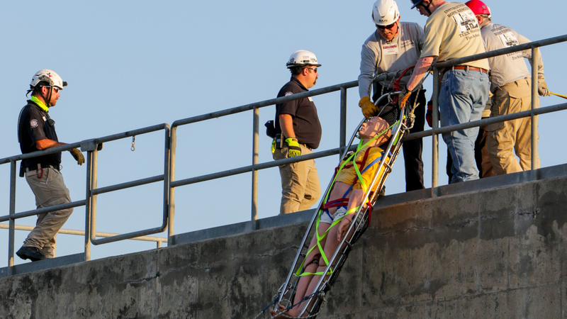 Firefighters working together during training to pull a dummy in a stretcher up a wall