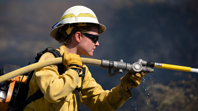 a side angle shot of a female firefighter carrying a hose over her shoulder