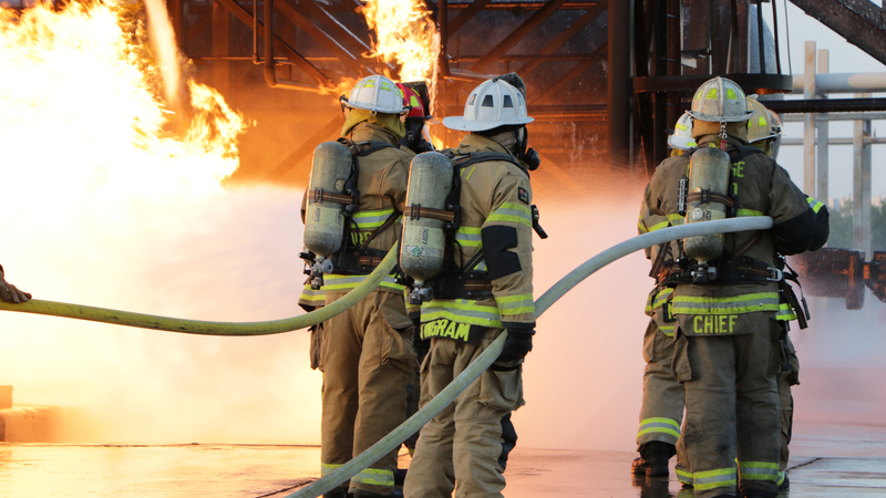 Three firefighters holding hoses as they fight a fire with water