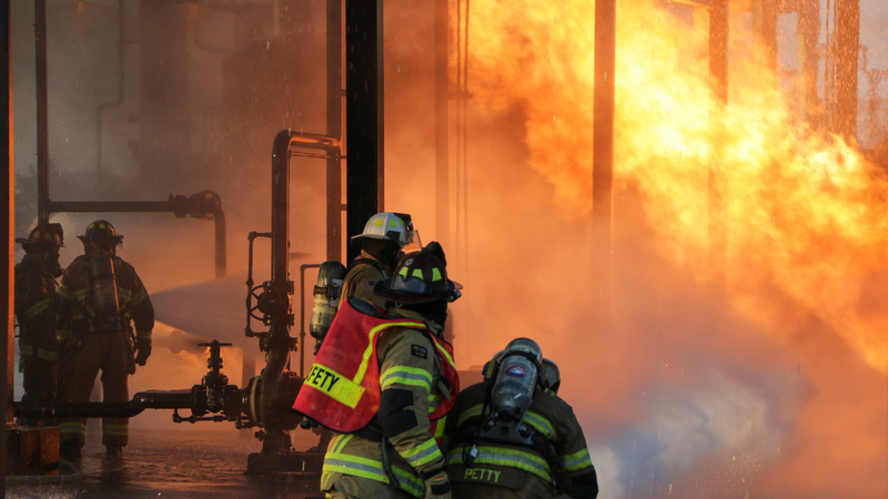 A group of firefighters fighting a roaring fire with water