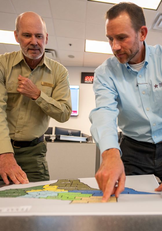 Two men pointing at a map of Texas laying on a table