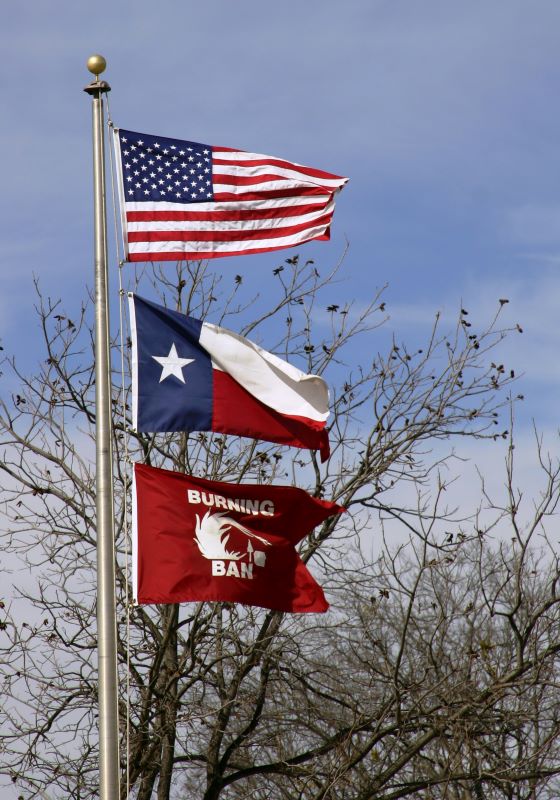 American flag, Texas flag, and burn ban flag flying on pole
