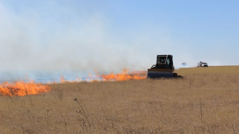 Grass field with fire burning and dozer