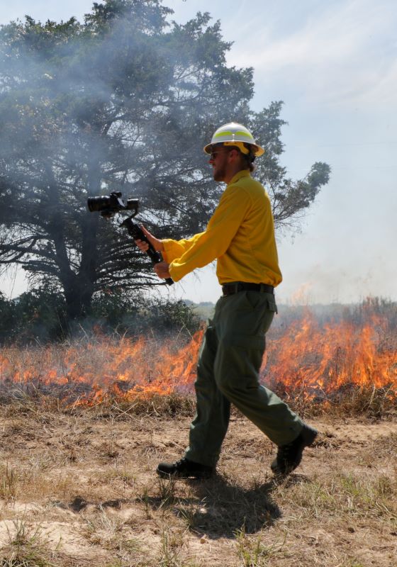 Firefighter walking in front of flames holding a video camera