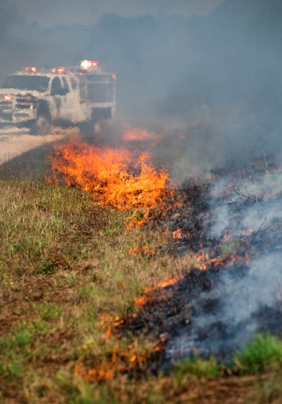 Fire burning in grass with smoke and a firetruck in the background