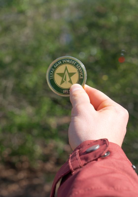 Hand holding a Texas A&M Forest Service coin