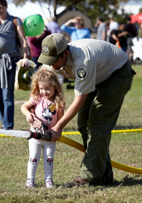 Young child spraying water hose with firefighters help