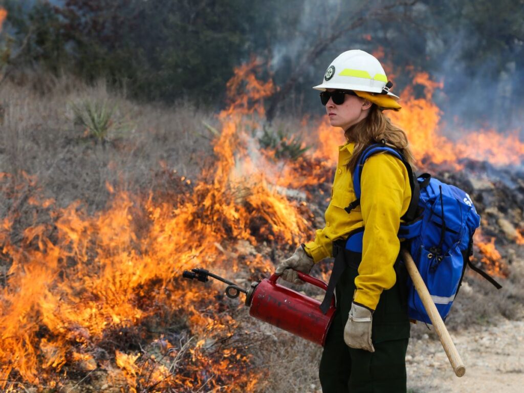Female firefighter standing with drip tourch in front of flames