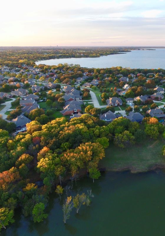Aerial view of houses surrounded by trees with a lake in the background