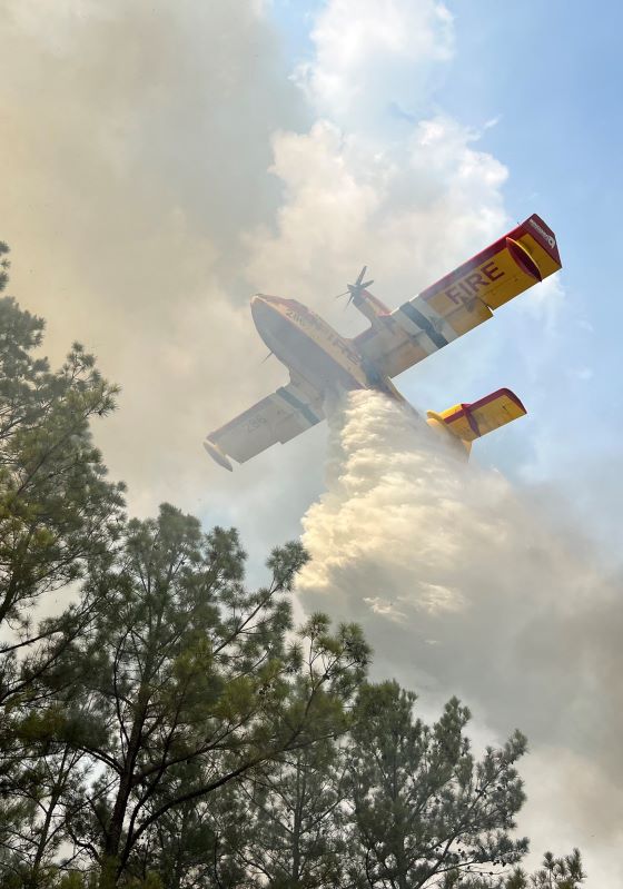 Large plane dropping water above trees smoking
