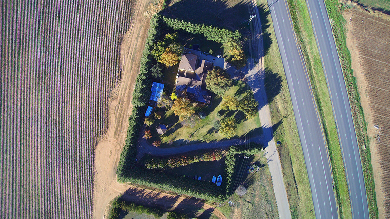 An aerial view of a property that is surrounded by trees that have been intentionally groan to create windbreak and provide shelter from the sun