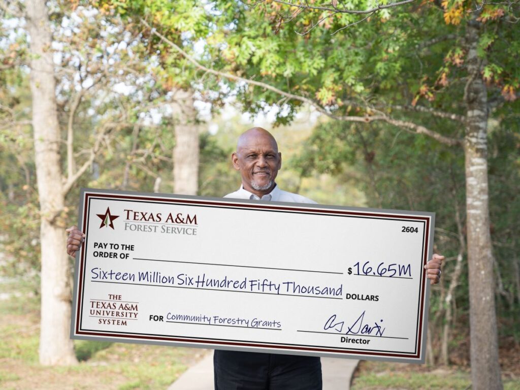 Al Davis holds large check made out for $16 million in front of green trees