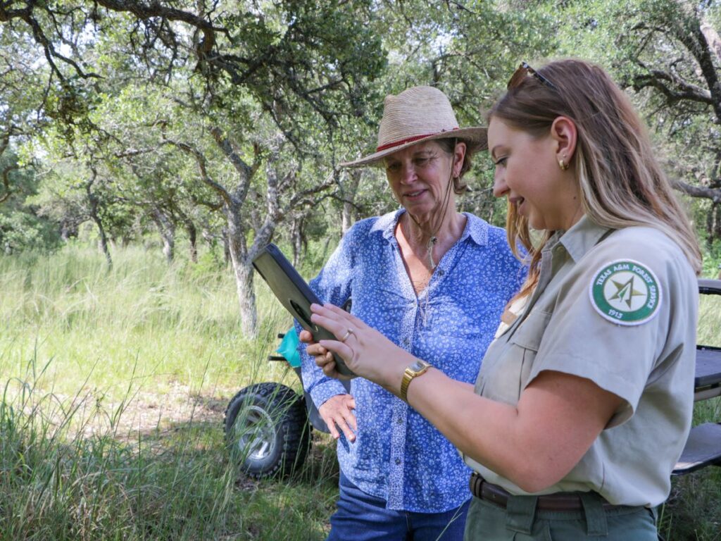 Forester and landowner look at ipad under trees