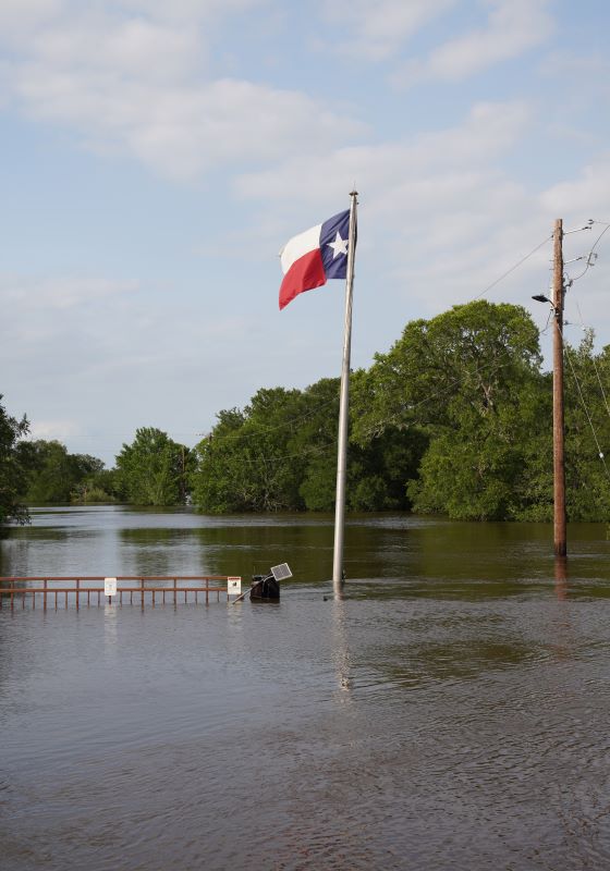 Flood waters reach top of gate with Texas flag flying in front of trees