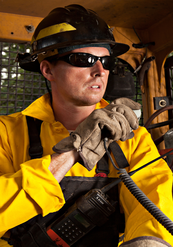 Firefighter in hard had and yellow shirt sits in dozer and holds up speaker