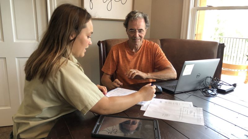 Forester sits with man at kitchen table with computer and paper