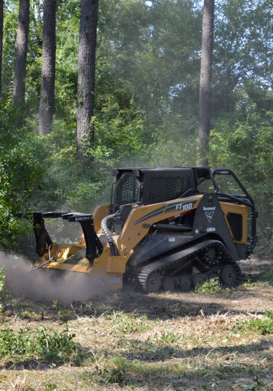 Yellow and black mulcher works in front of pine trees