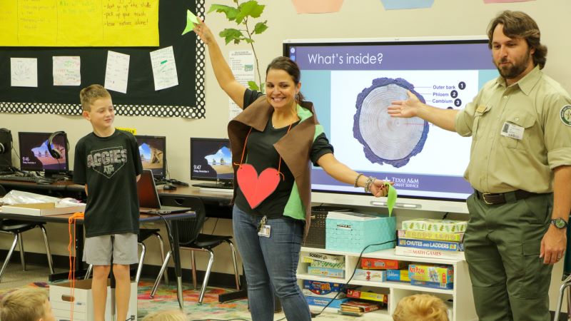 Teacher standing in front of classroom dressed like a tree with a forester pointing
