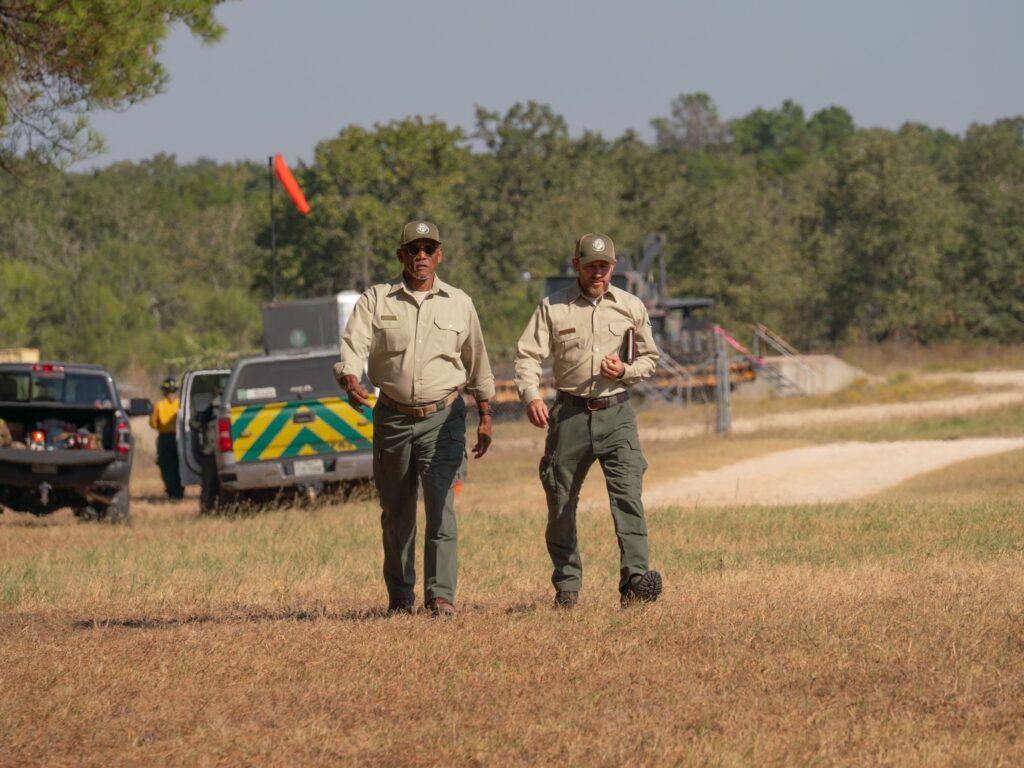 Two foresters walk through field with trucks behind them