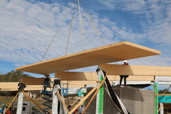 Construction lowering a large piece of wood onto wooden beams