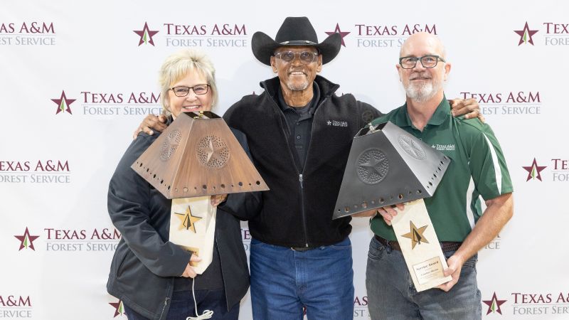 Two awardees stand holding large lamps with Director Al Davis