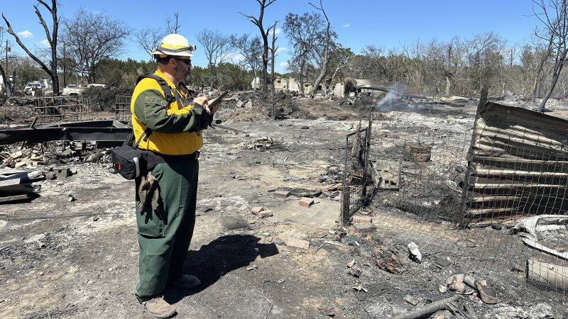 Firefighter conducting a post-fire assessment in a burned area holding an ipad.